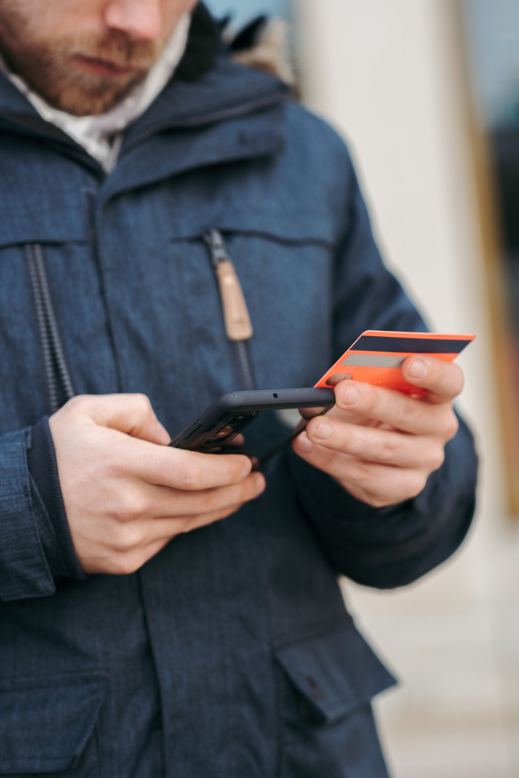 Crop unrecognizable bearded male in warm outerwear entering credit cards details while making online payment via mobile phone on street